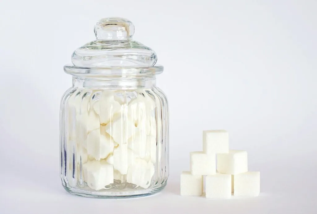 Bocal en verre rempli de sucres en morceaux, à côté d'une pyramide de sucres