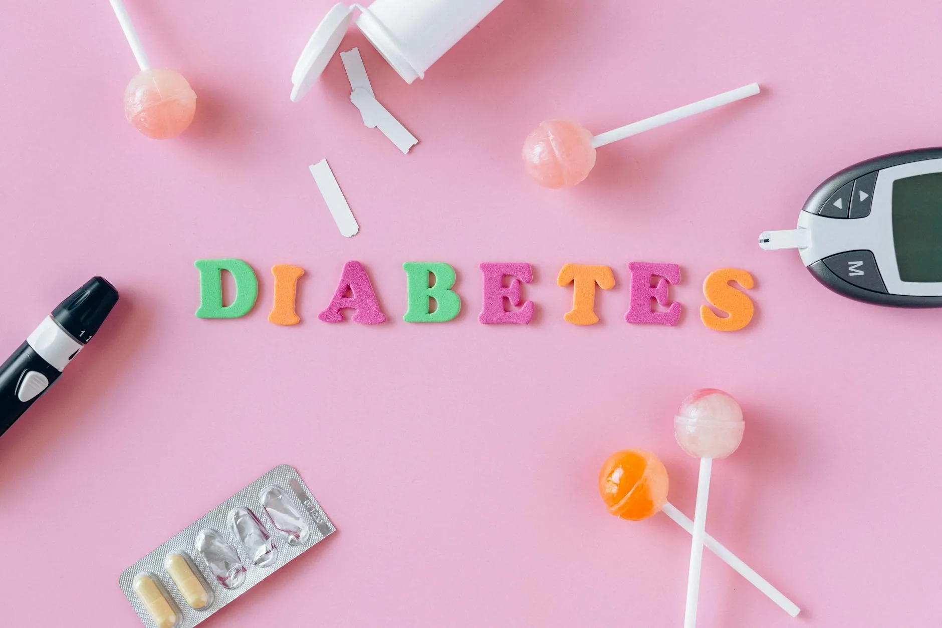 Flat lay image depicting diabetes with glucometer, pills, and lollipops on a pink background.