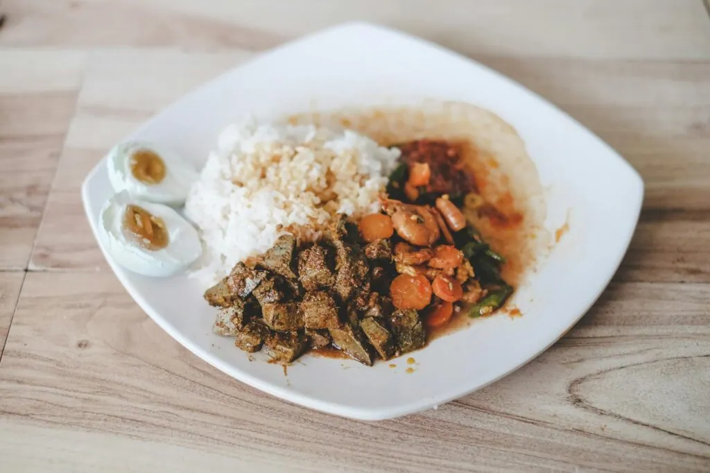 Assiette de riz, foie en sauce, légumes et œuf dur sur une table en bois